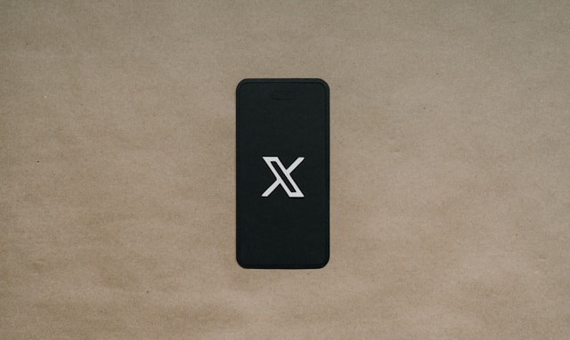 Un teléfono negro sobre una superficie marrón que muestra el logotipo X.