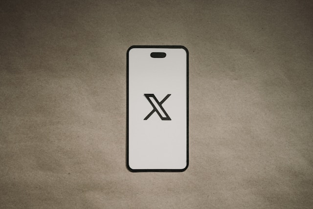 Casing ponsel berwarna putih menampilkan logo X pada latar belakang cokelat.