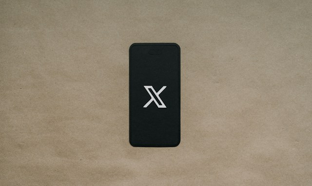 Una foto di un telefono posizionato su uno sfondo marrone che mostra il logo X sullo schermo.