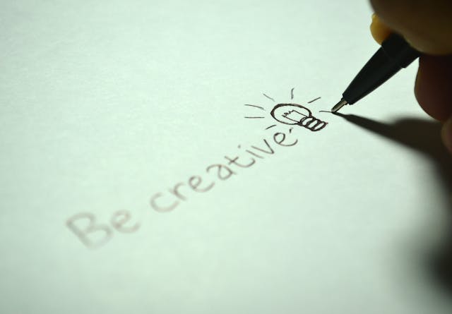誰かがペンで紙に「BE CREATIVE」と書く。
