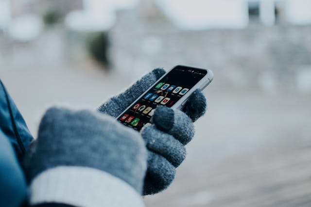 Een persoon die een smartphone gebruikt en winterhandschoenen draagt.