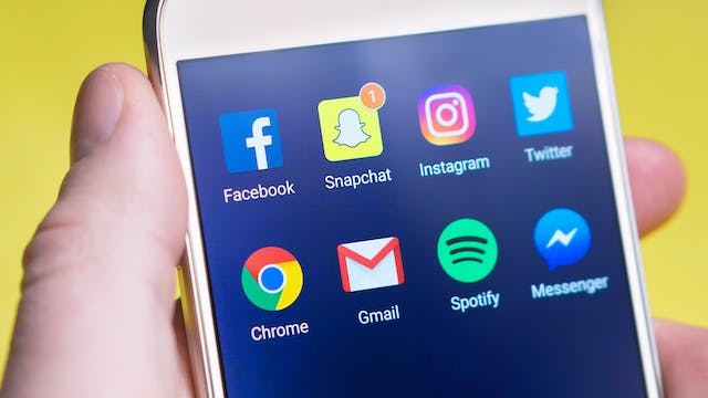 Imagem em grande plano de uma mão a segurar um telemóvel que mostra um separador social com aplicações de redes sociais.