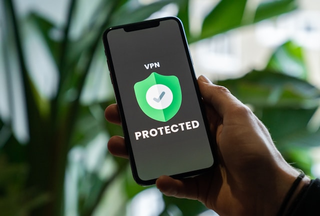 Uma mão segura um telemóvel e o ecrã mostra um crachá com as palavras "VPN PROTECTED".