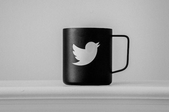 A photograph of a black cup on a table designed with Twitter’s bird logo in white.