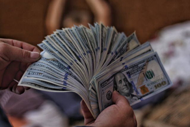 A person holds several $100 U.S. bank notes in their hands.