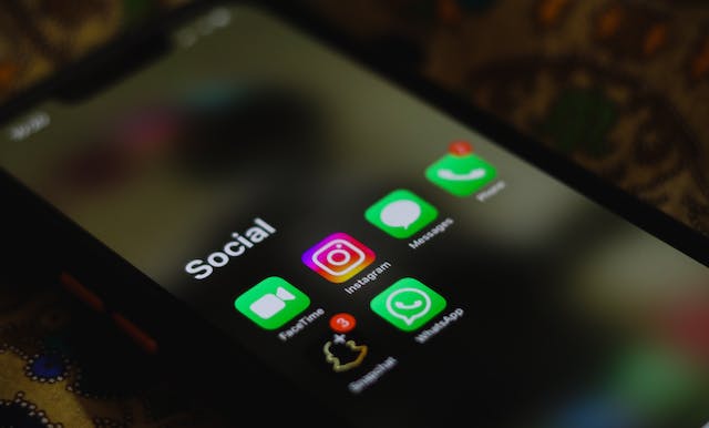 O ilustrație de like-uri de social media, cutii de mesaje și pictograme de profil în jurul unui smartphone albastru pe o platformă albă.